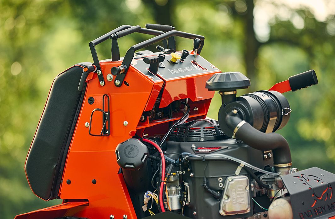Orange and black tracked stump grinder machine outdoors with engine components.