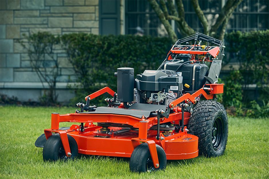Orange zero-turn lawnmower on green grass, in front of a house.