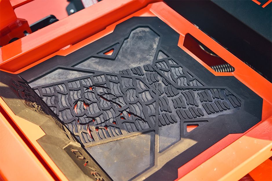 Black rubber mat inside an orange machine, textured surface with a pattern resembling overlapping tiles.