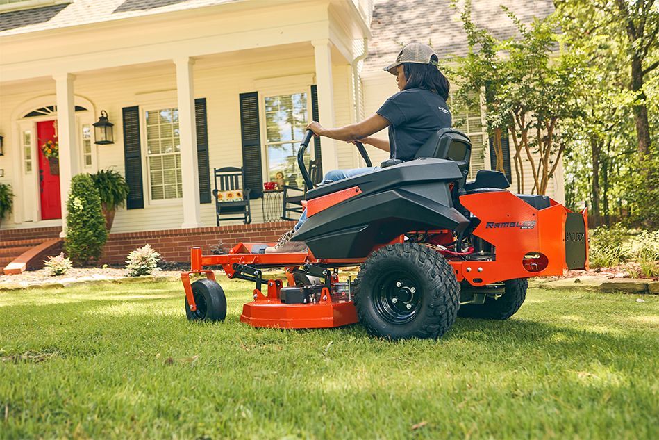 Woman mowing lawn with orange riding mower in front of a white house.