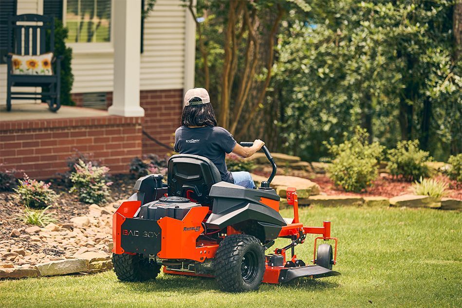 Person mowing lawn on a bright orange riding mower in front yard.