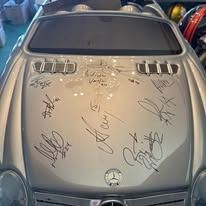 The hood of a silver car is covered in signatures.