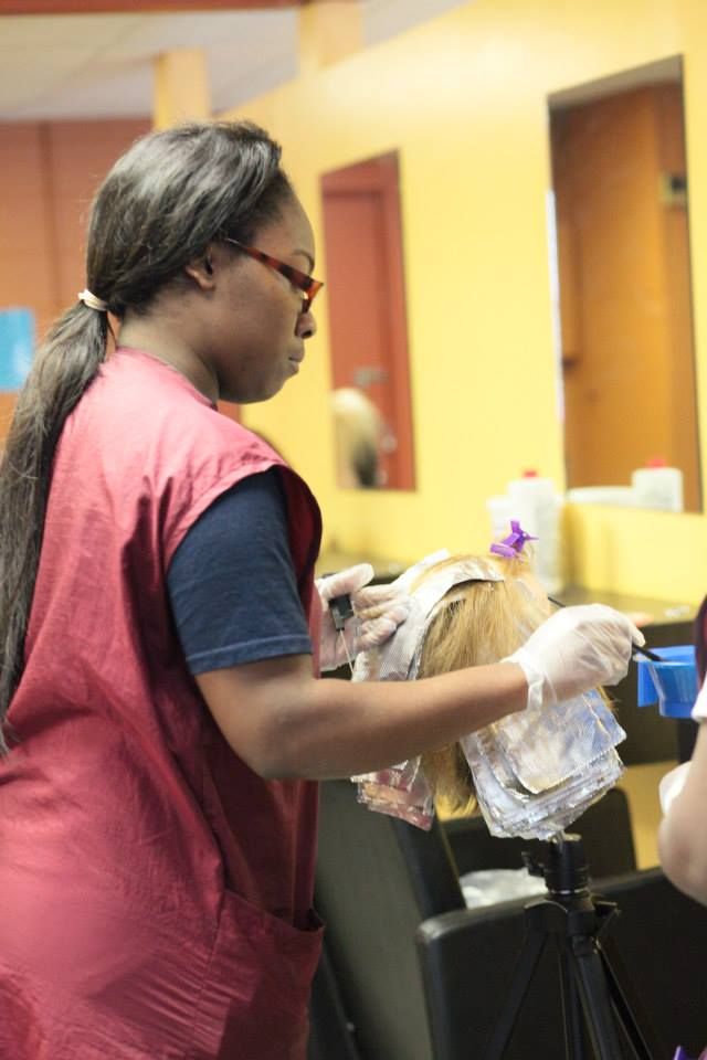 Person with glasses applying hair dye in salon.