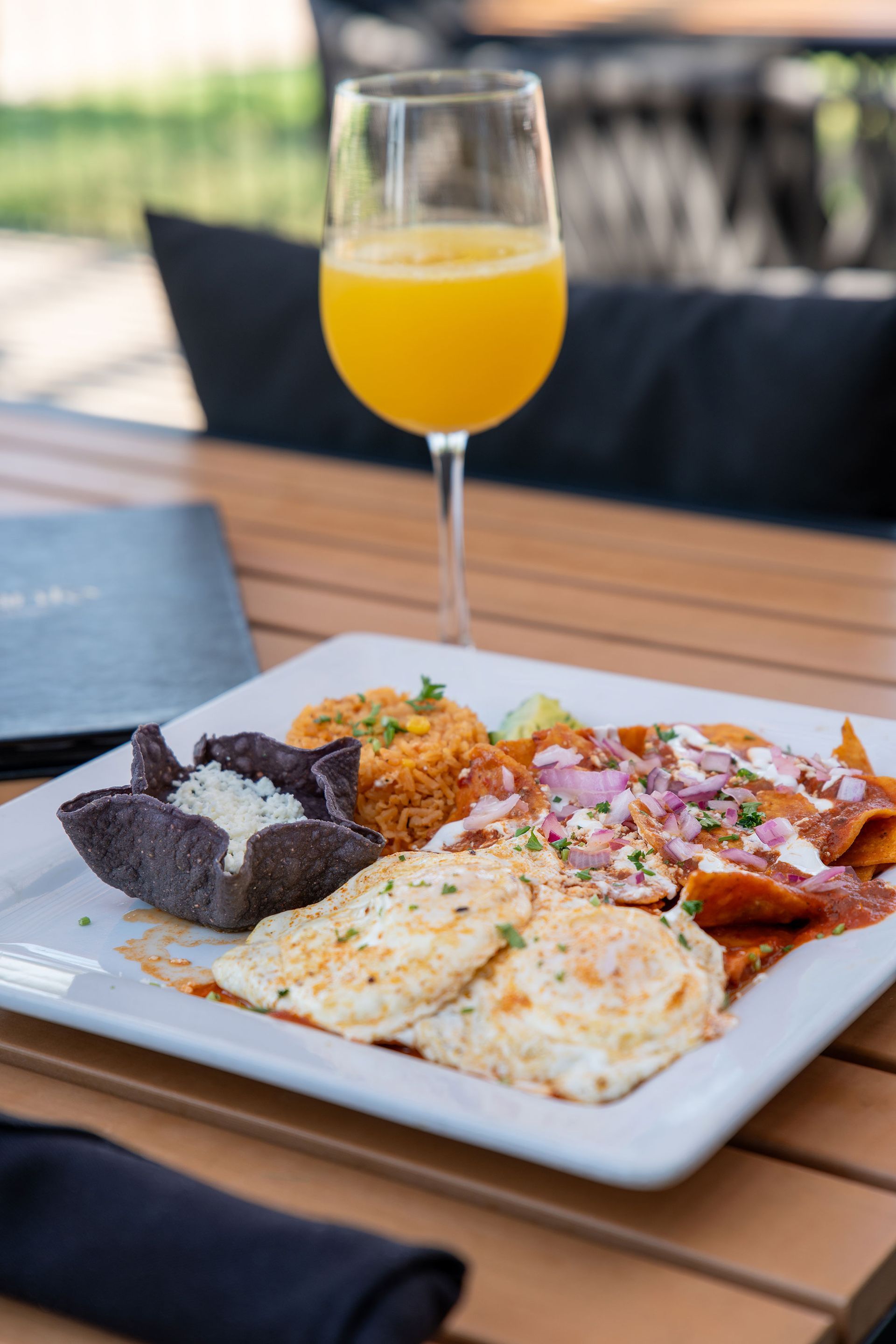 Plate of food: enchiladas, rice, eggs, salsa, and a mimosa on a wooden table.