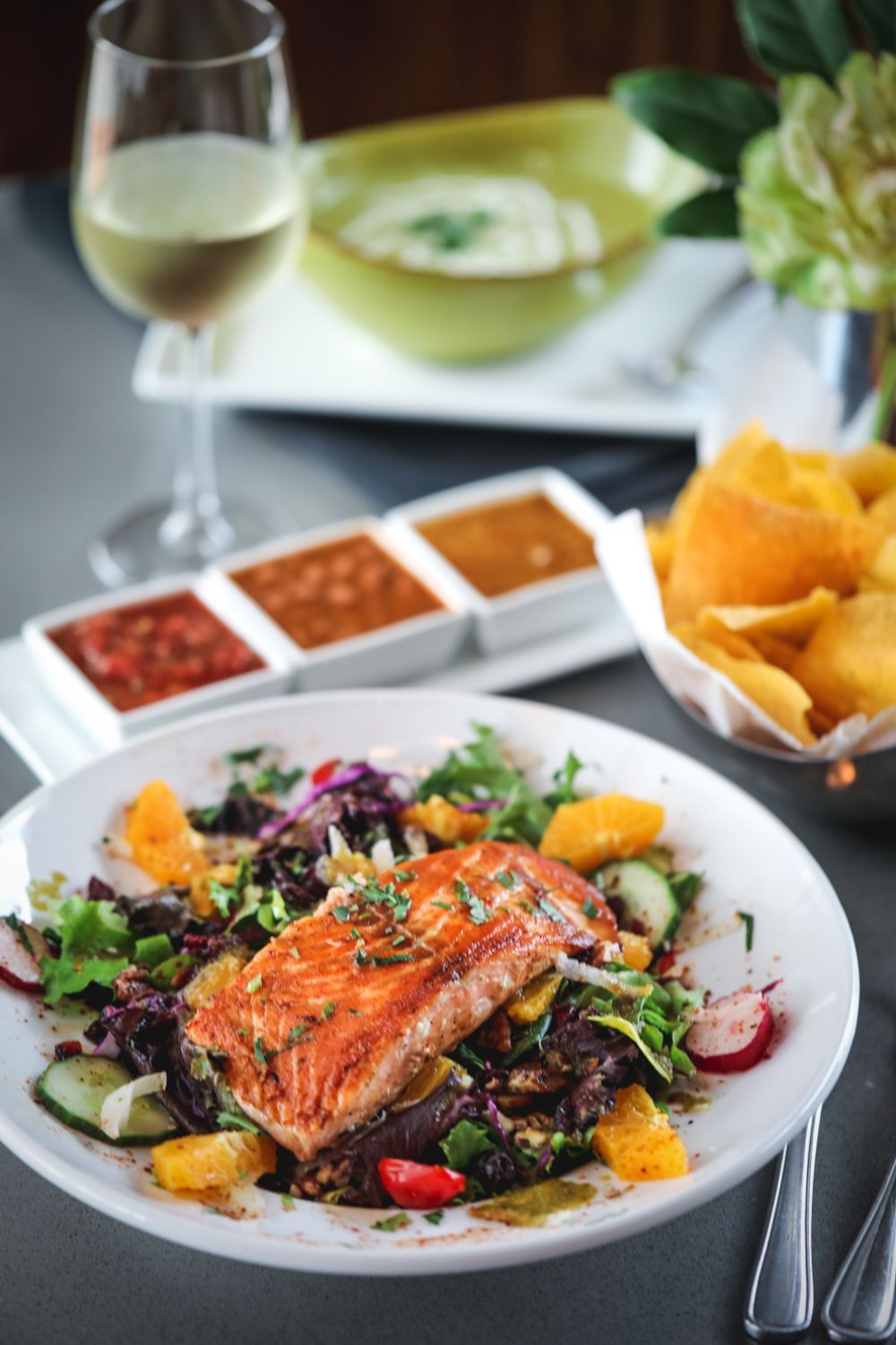 Salmon salad with citrus, dips, chips, wine glass.