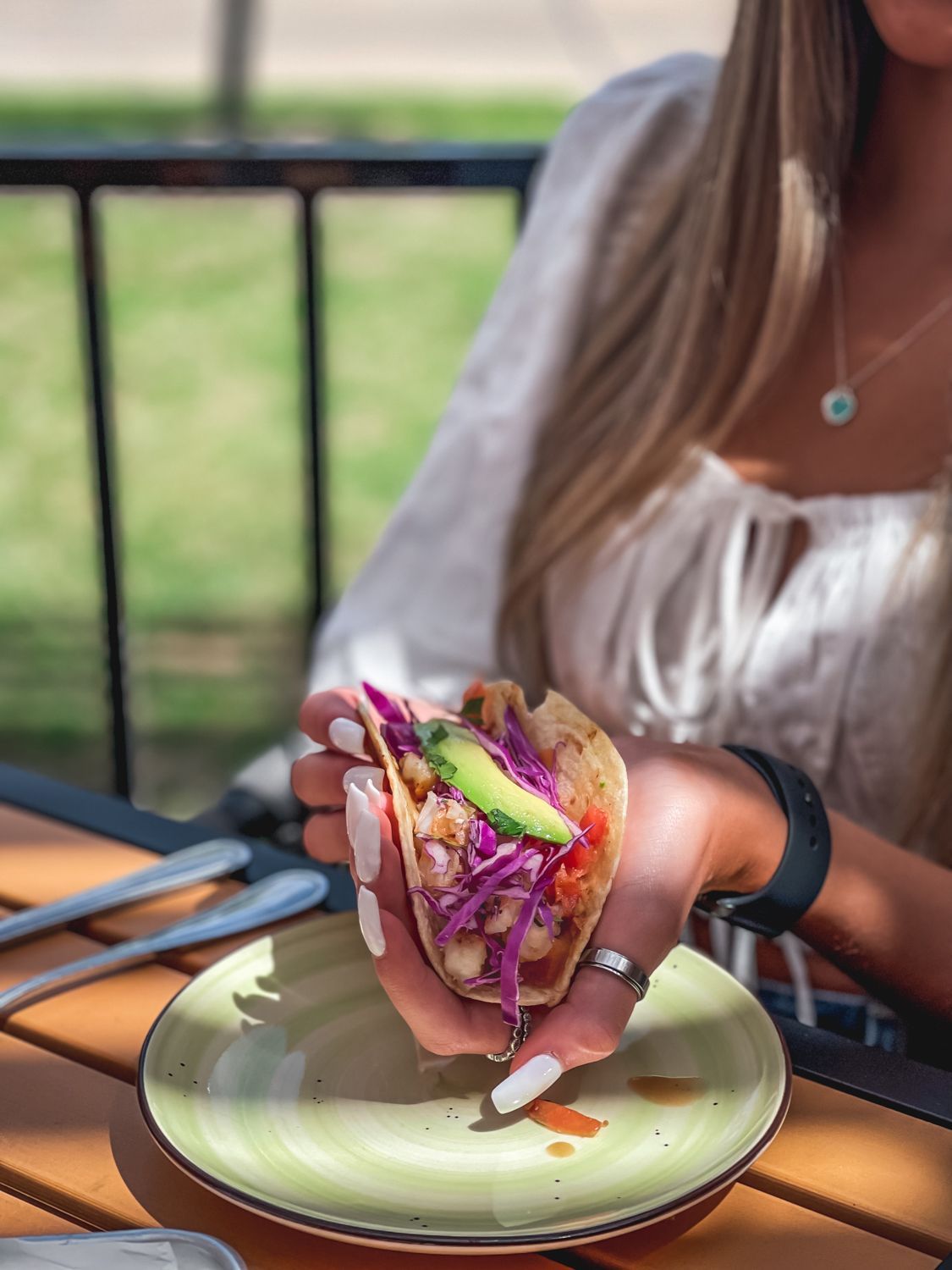 Woman holding a taco with red cabbage, avocado, and salsa. Taco on a plate on a wooden table.