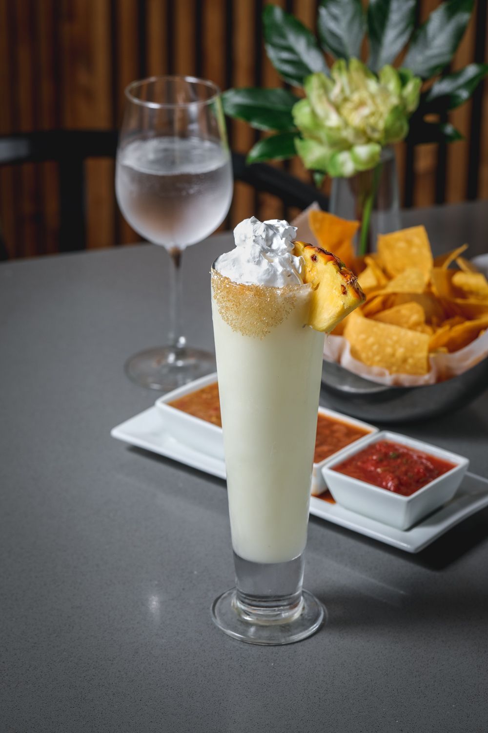 Tall cocktail with whipped cream, chips and salsa, water glass.