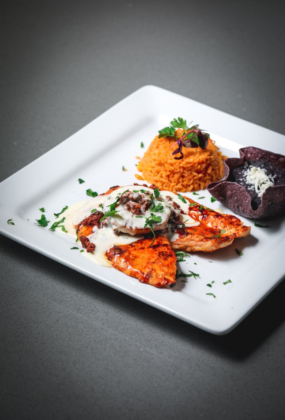 Plate of food: chicken with sauce, orange rice, purple chips, garnished with parsley.