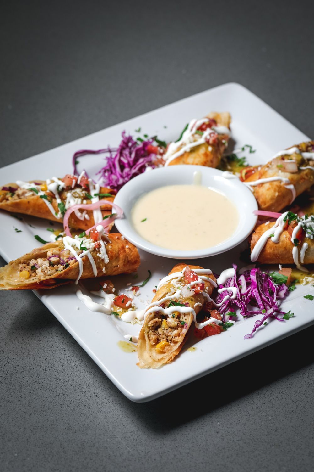 Plate of fried egg rolls with dipping sauce, garnished with salsa, parsley, and purple cabbage.