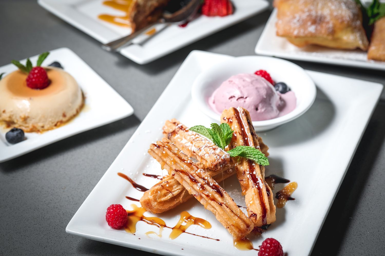 Dessert dishes on white plates: churros with ice cream, flan, and a pastry.