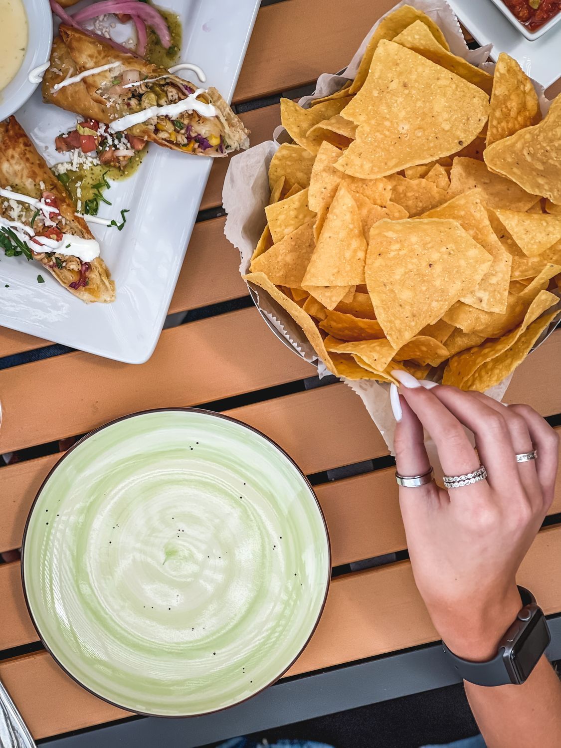 Overhead shot of restaurant table with nachos, appetizers, and a hand reaching for a chip.