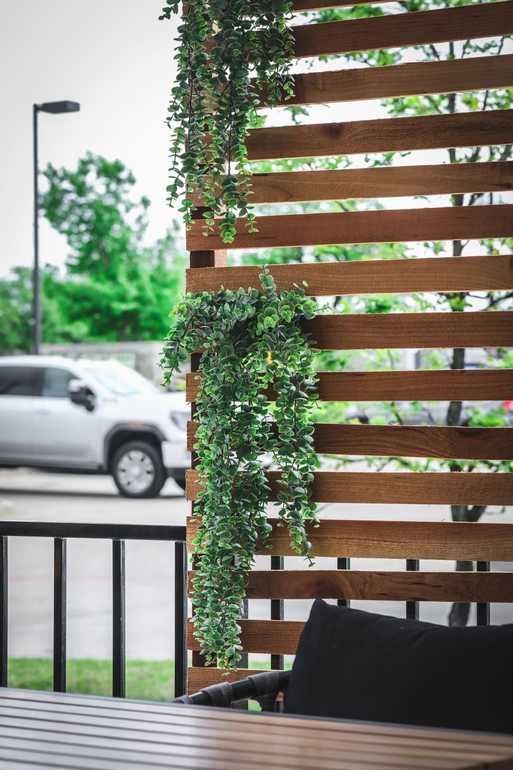 Wooden slatted privacy screen with hanging greenery; car and street lamp in the background.