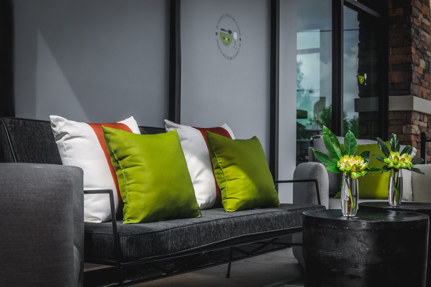 Outdoor seating area: gray sofa with green and white pillows, black side table, and plant display.