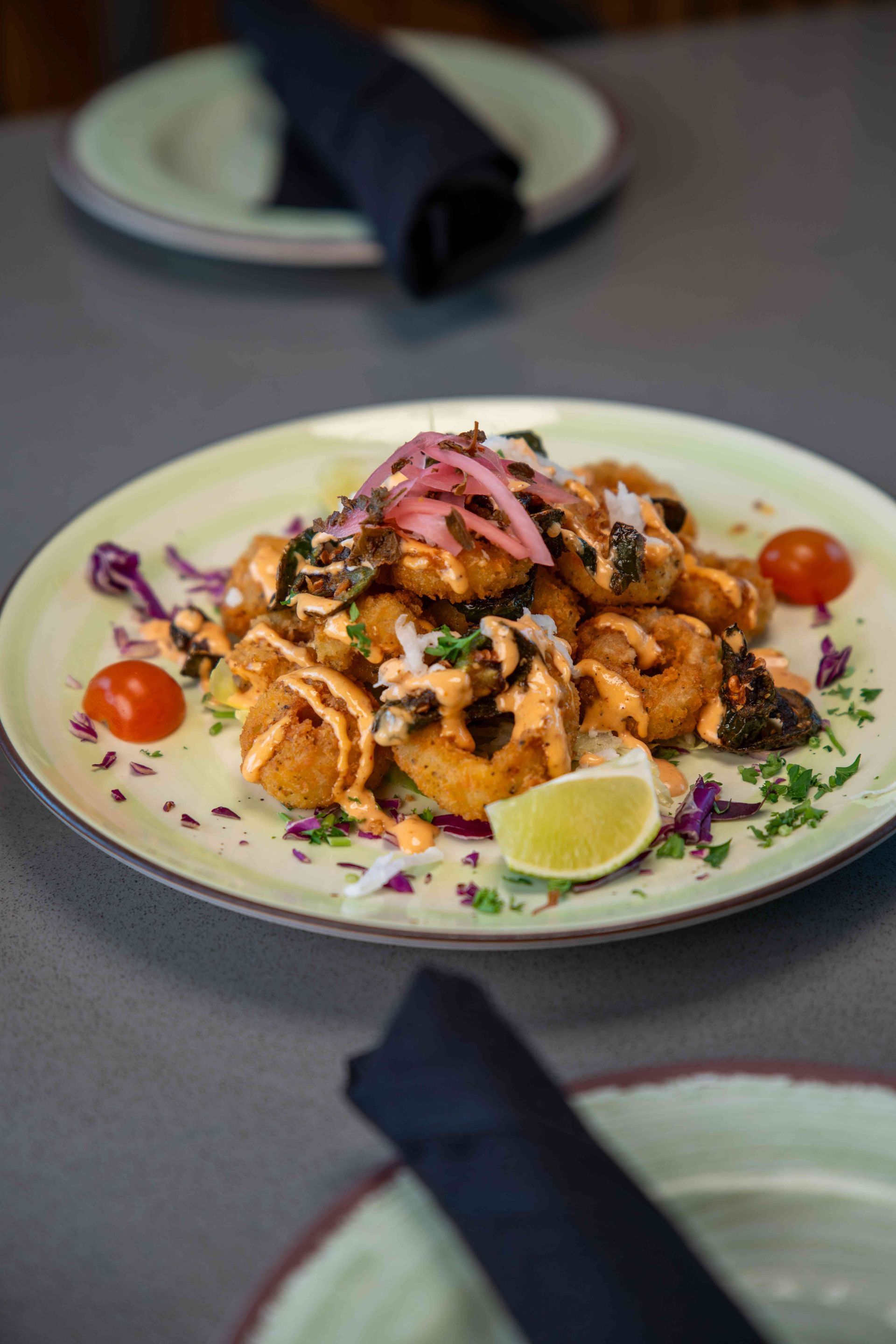 Fried calamari with sauce, pickled onions, and lime wedge on a plate, set on a table.