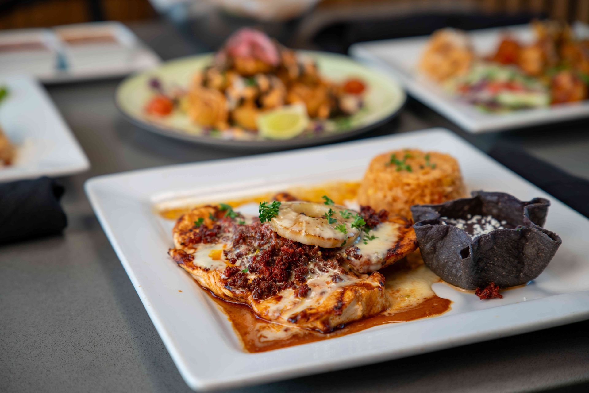 Plate of Mexican food: chicken with sauce, rice, black bean bowl, plus other dishes in background.