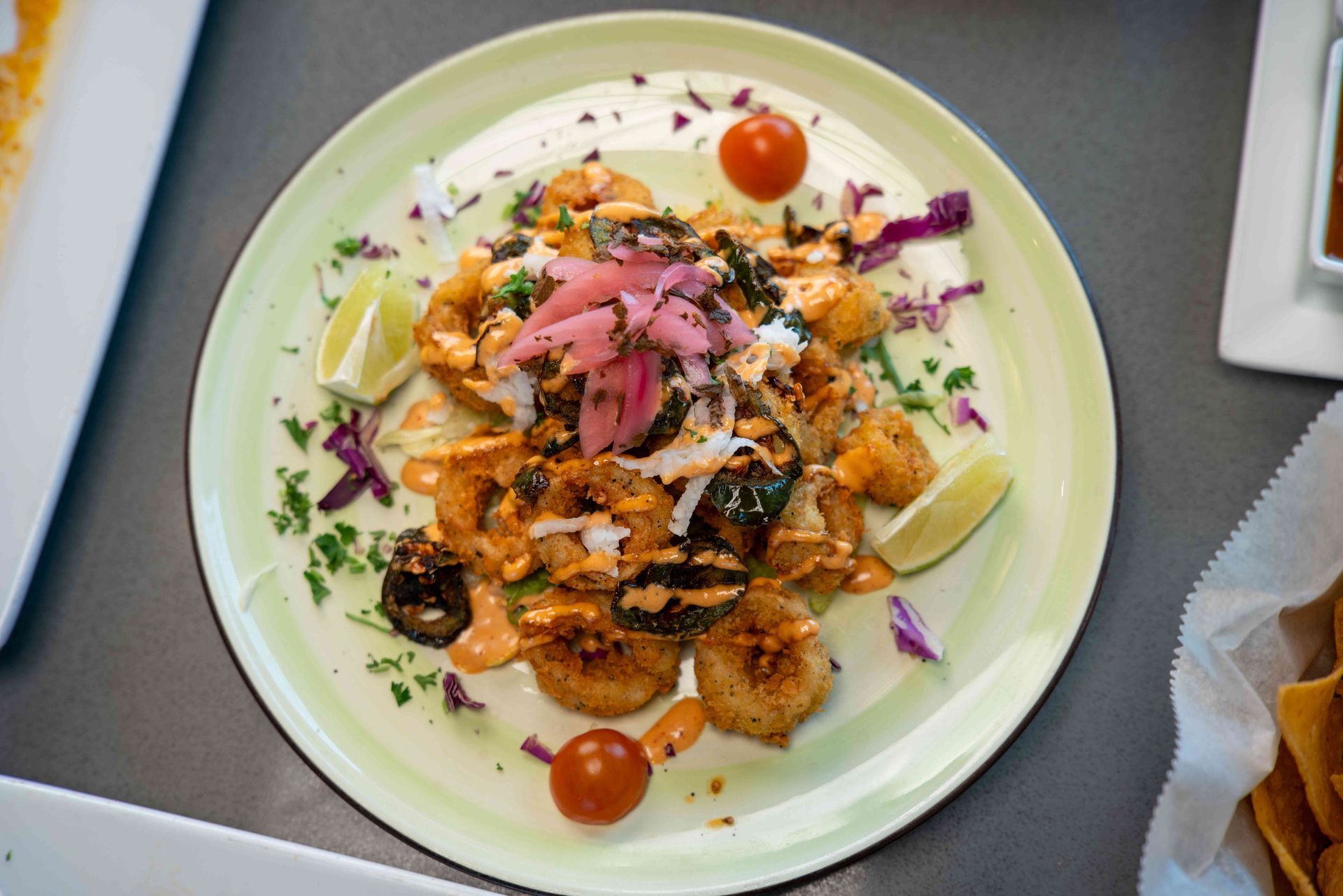 Seared scallops and fried tofu on a green plate, topped with pickled onions, salsa, and tomatoes, with lime wedges.