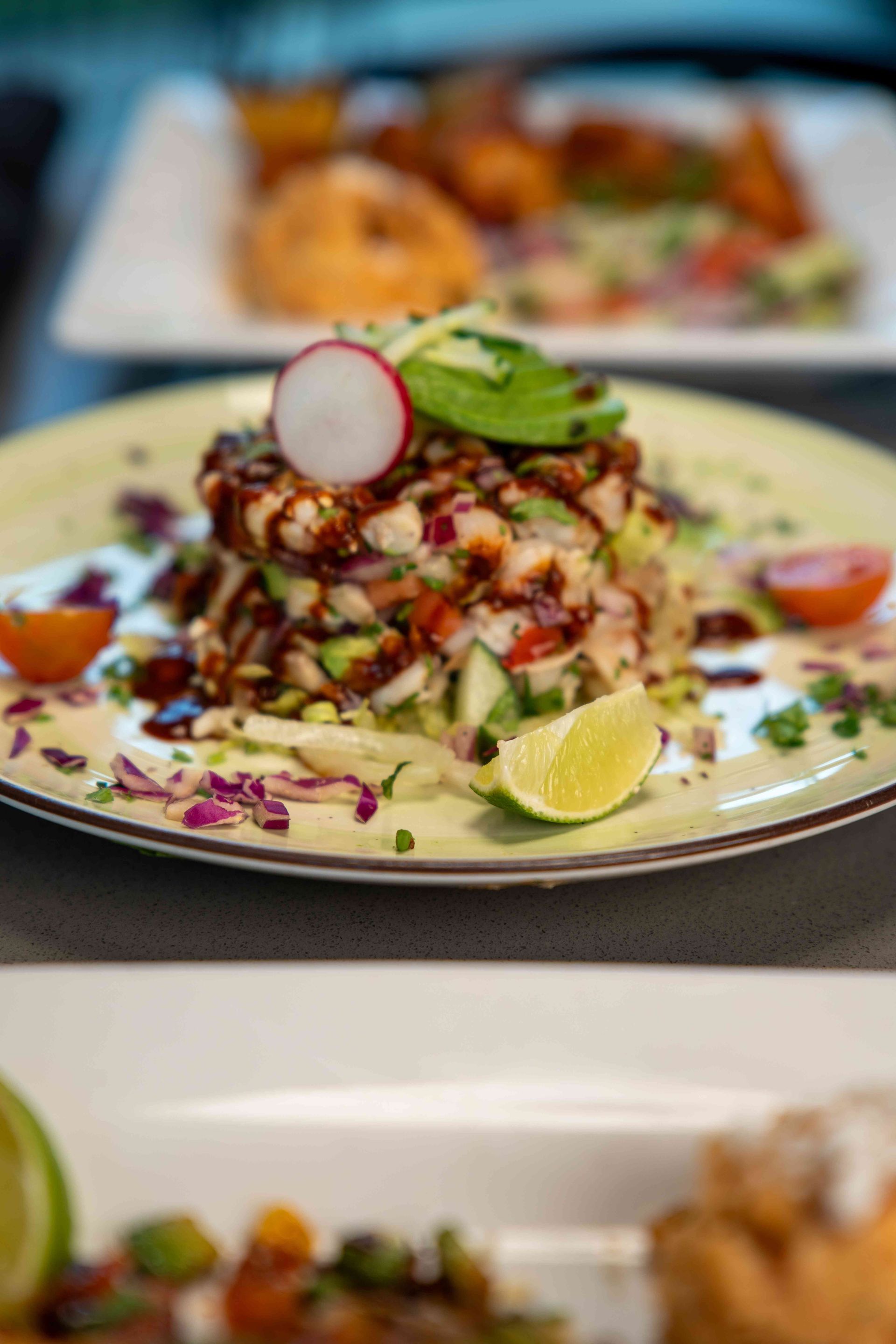 Seafood ceviche stacked high on a plate, garnished with avocado, radish, and lime.