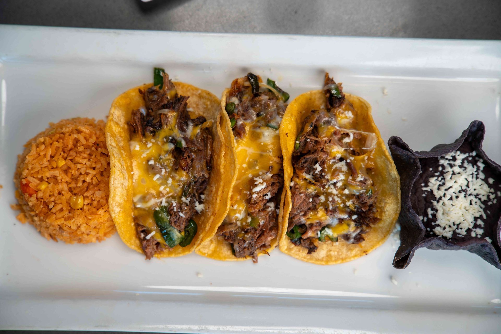 Three stuffed pepper tacos with rice and beans on a rectangular white plate.