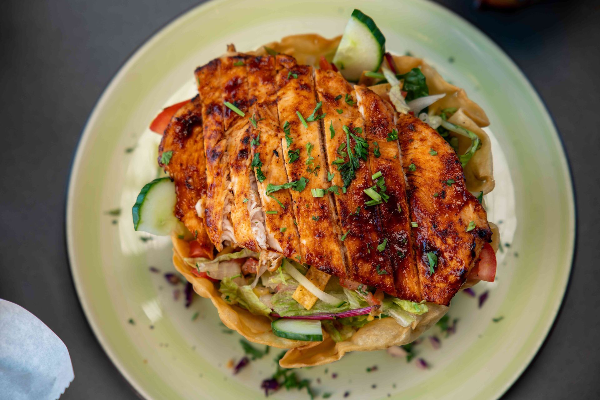 Grilled chicken salad in a fried tortilla bowl with cucumbers and herbs.