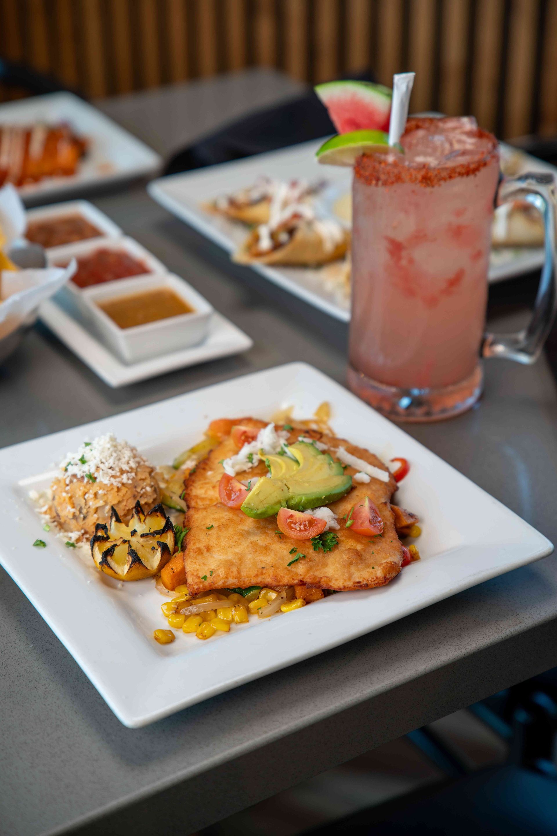 Plate of food with avocado and drink with lime and watermelon garnish on a table.
