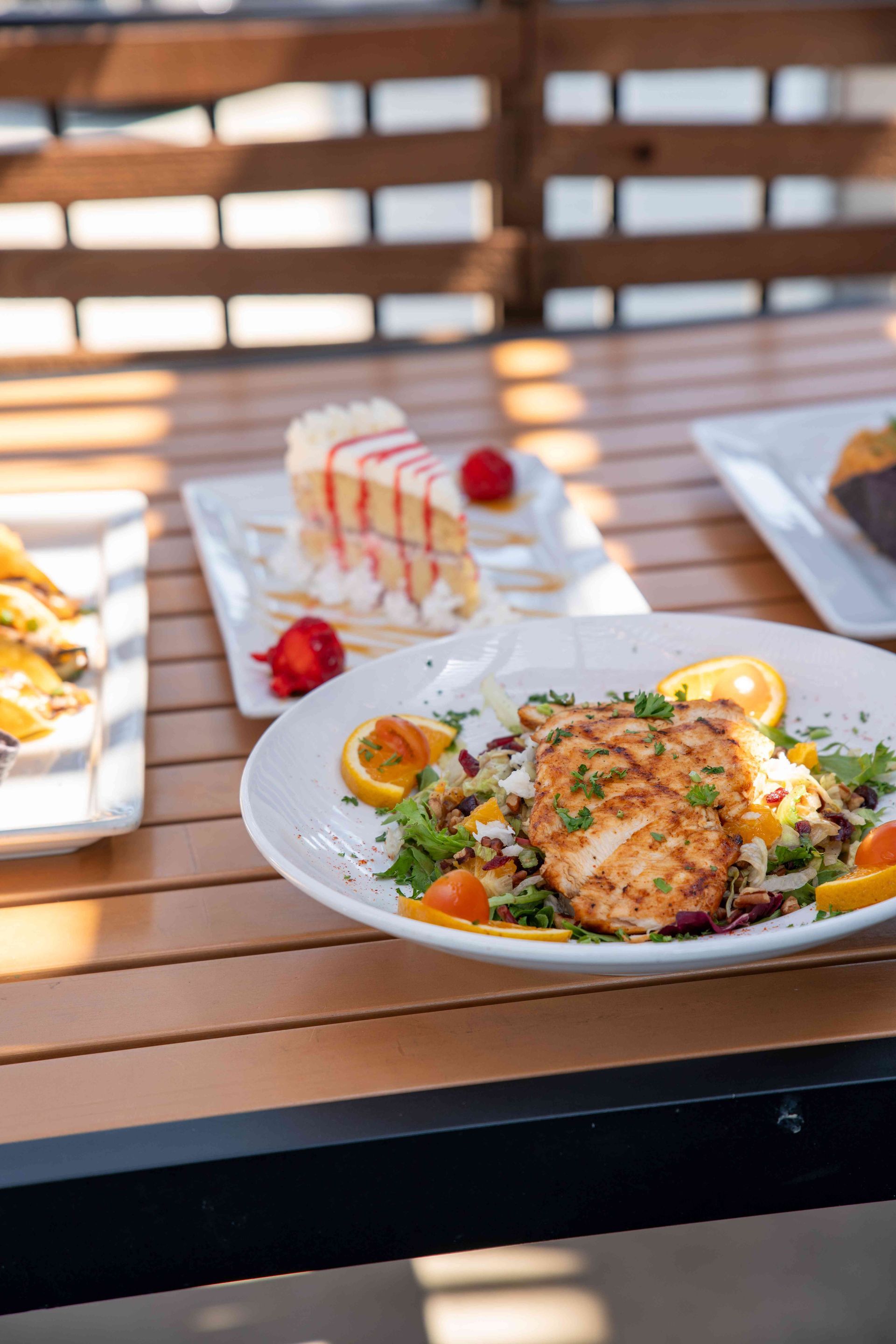 A plate of food with fish and orange slices on a wooden table with desserts nearby.