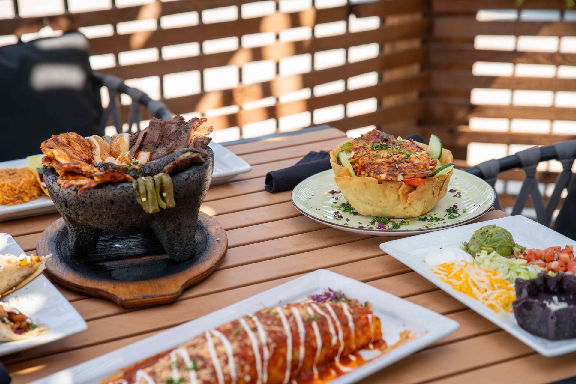 Mexican food spread on a wooden table, including a molcajete, burrito, and taco salad.
