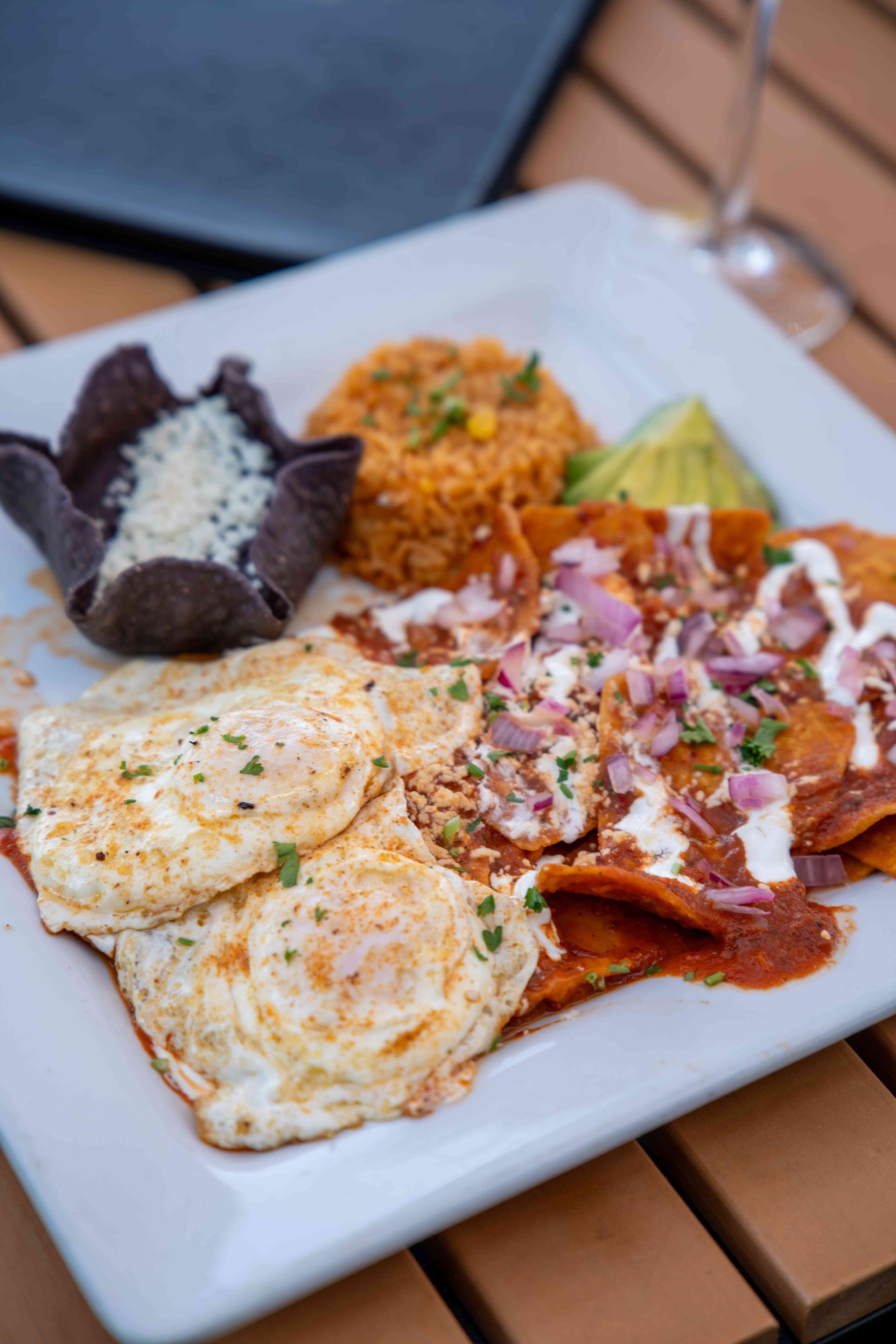 Plate of chilaquiles with fried eggs, rice, beans, lime, and red onions.