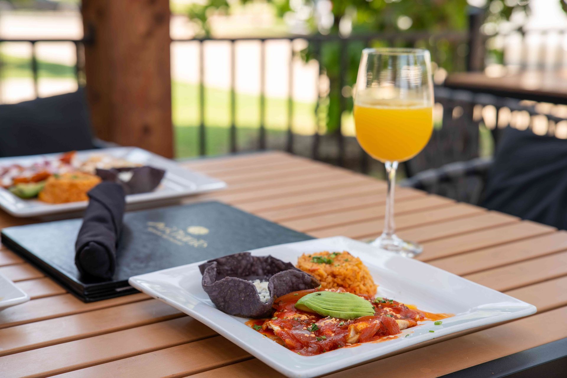 Outdoor table with plate of food, rice, avocado, drink, and menu.