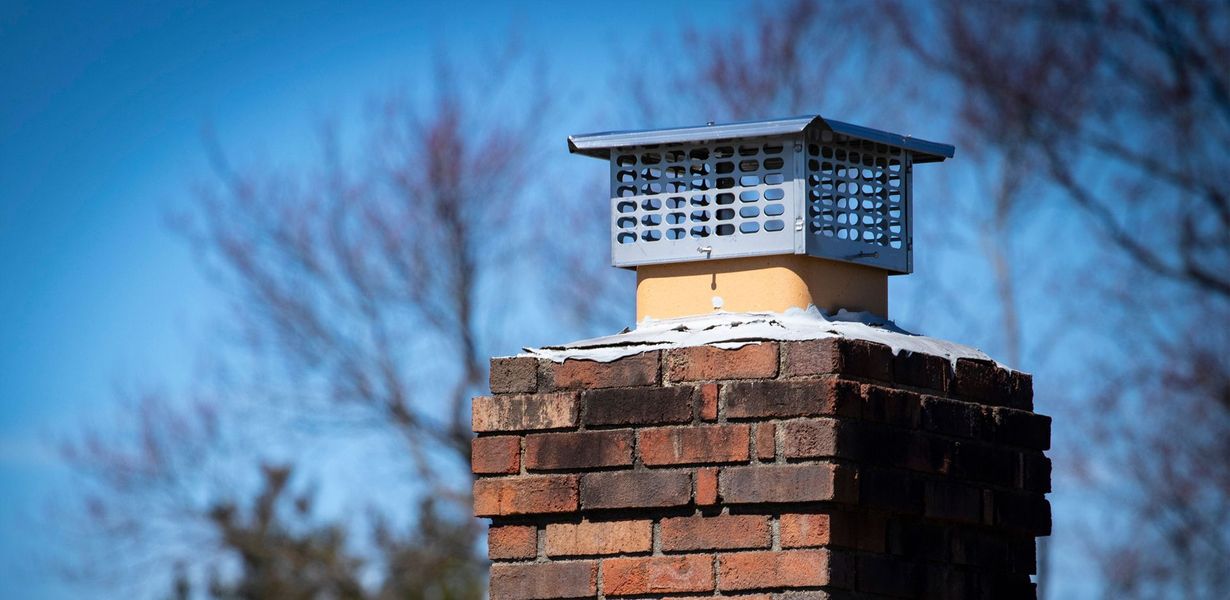 A brick chimney topped with a metal cover, standing against a clear sky.
