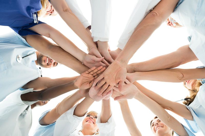 Medical team with hands joined in a circle, looking up, smiling.