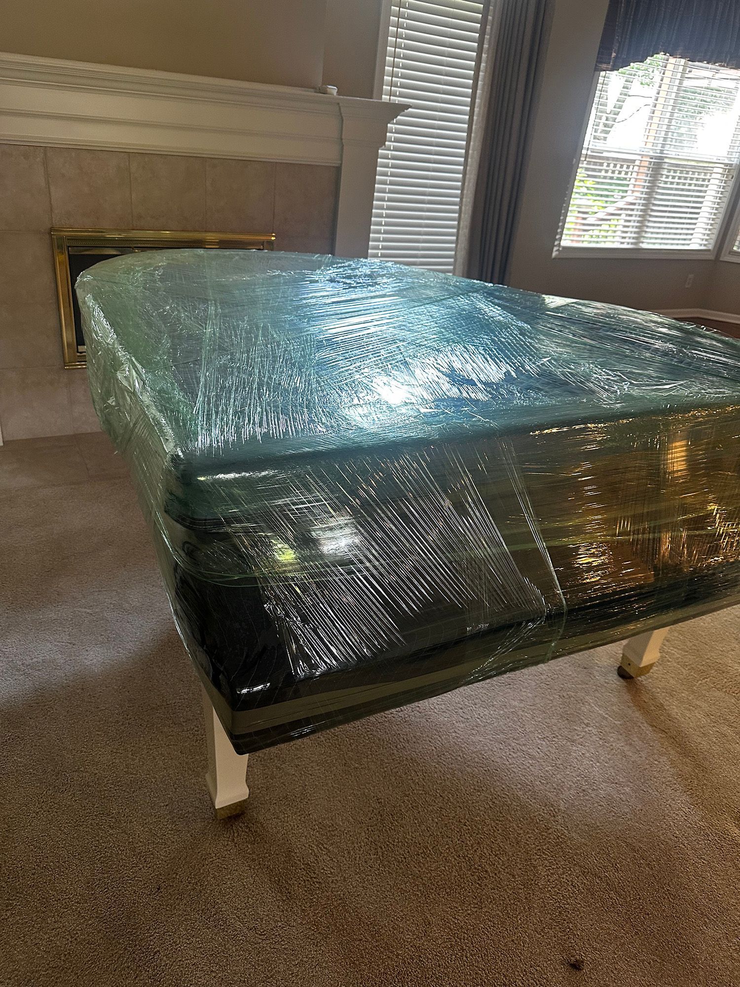 A large rectangular object, possibly a mattress or table, wrapped in clear plastic, rests on white legs.