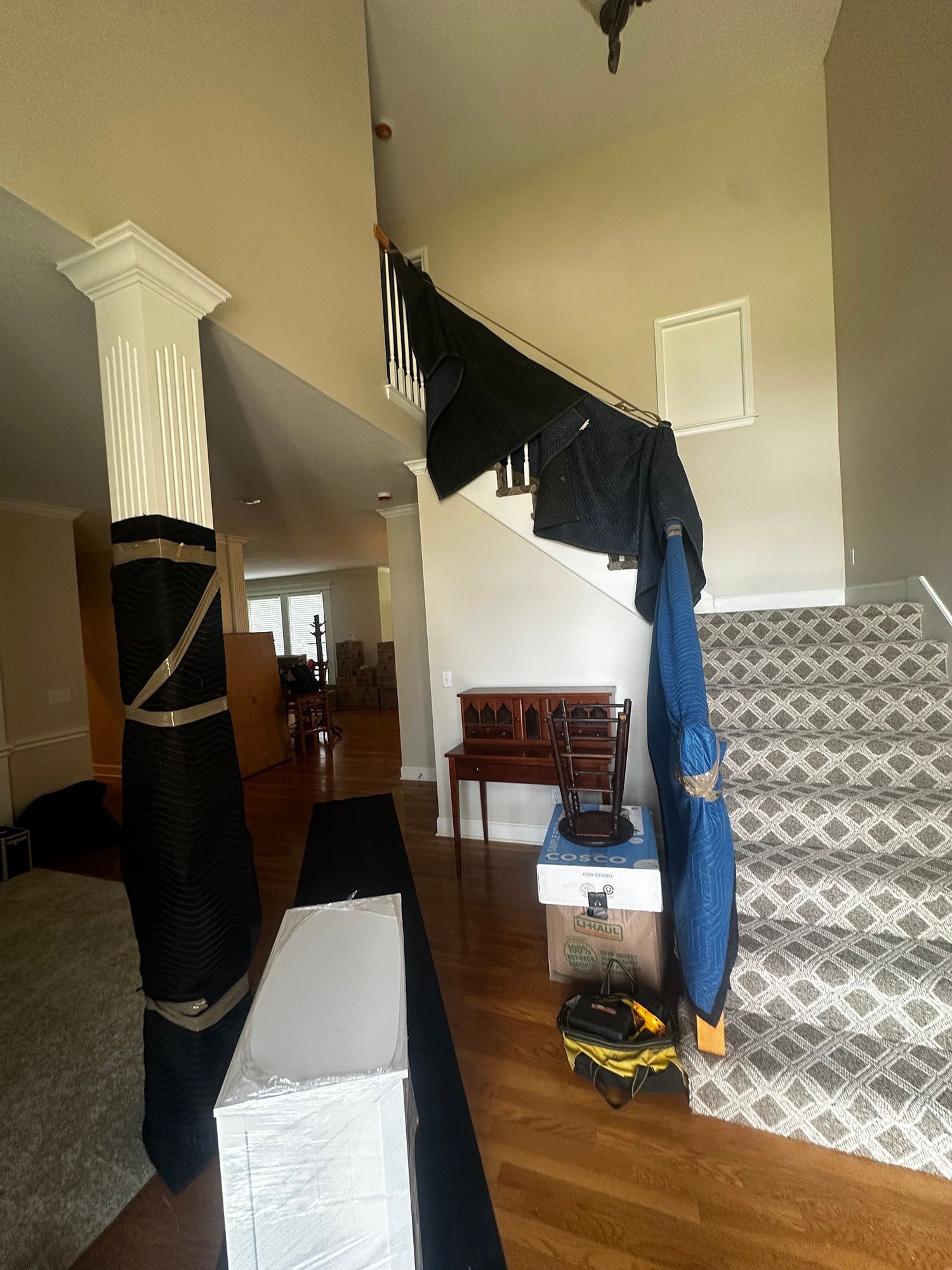 View from above a staircase and into a home. A black tarp is draped over the railing. A white column and a wooden desk are visible.