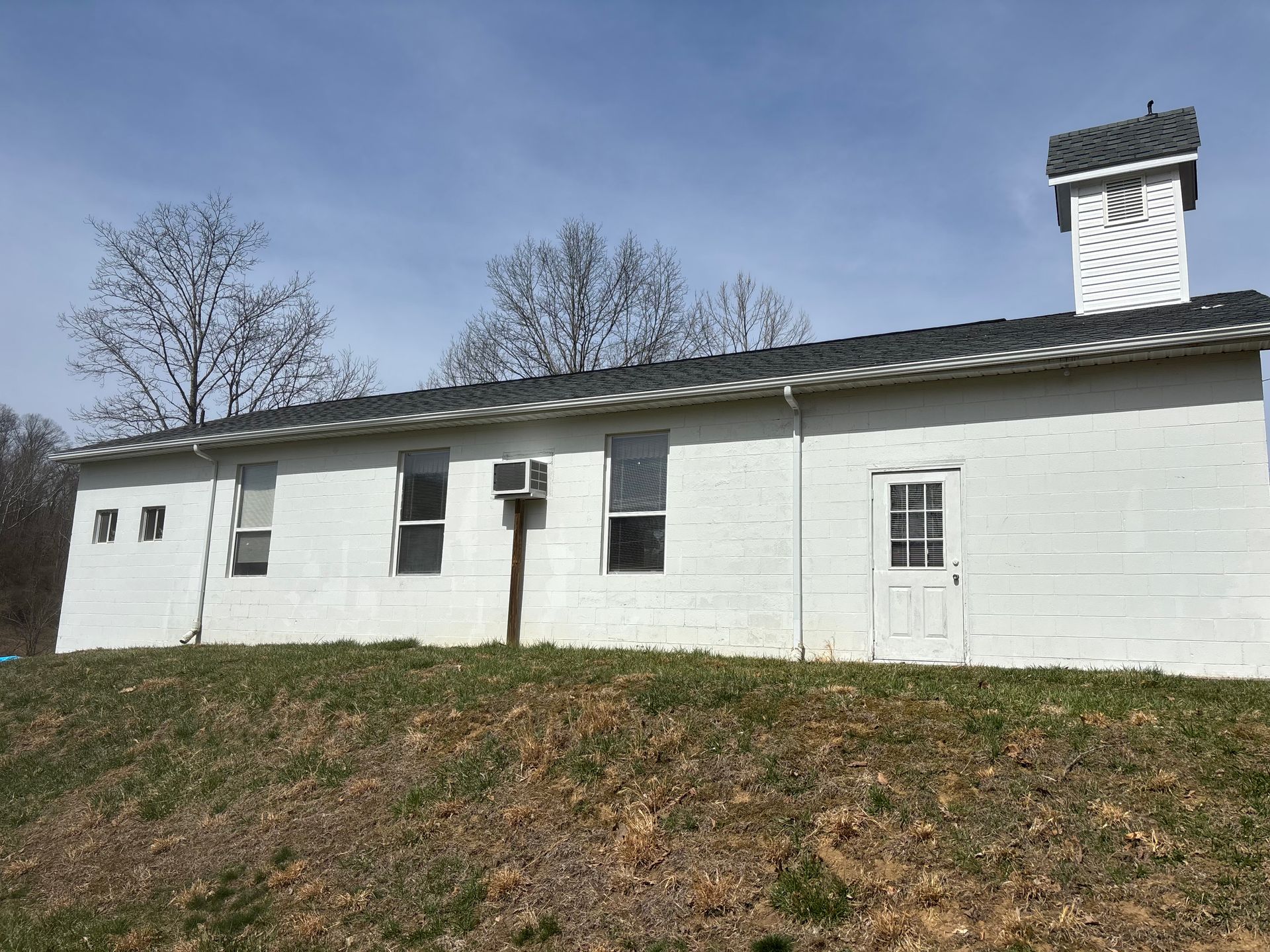 A white building with a clock tower on top of it is sitting on top of a grassy hill.