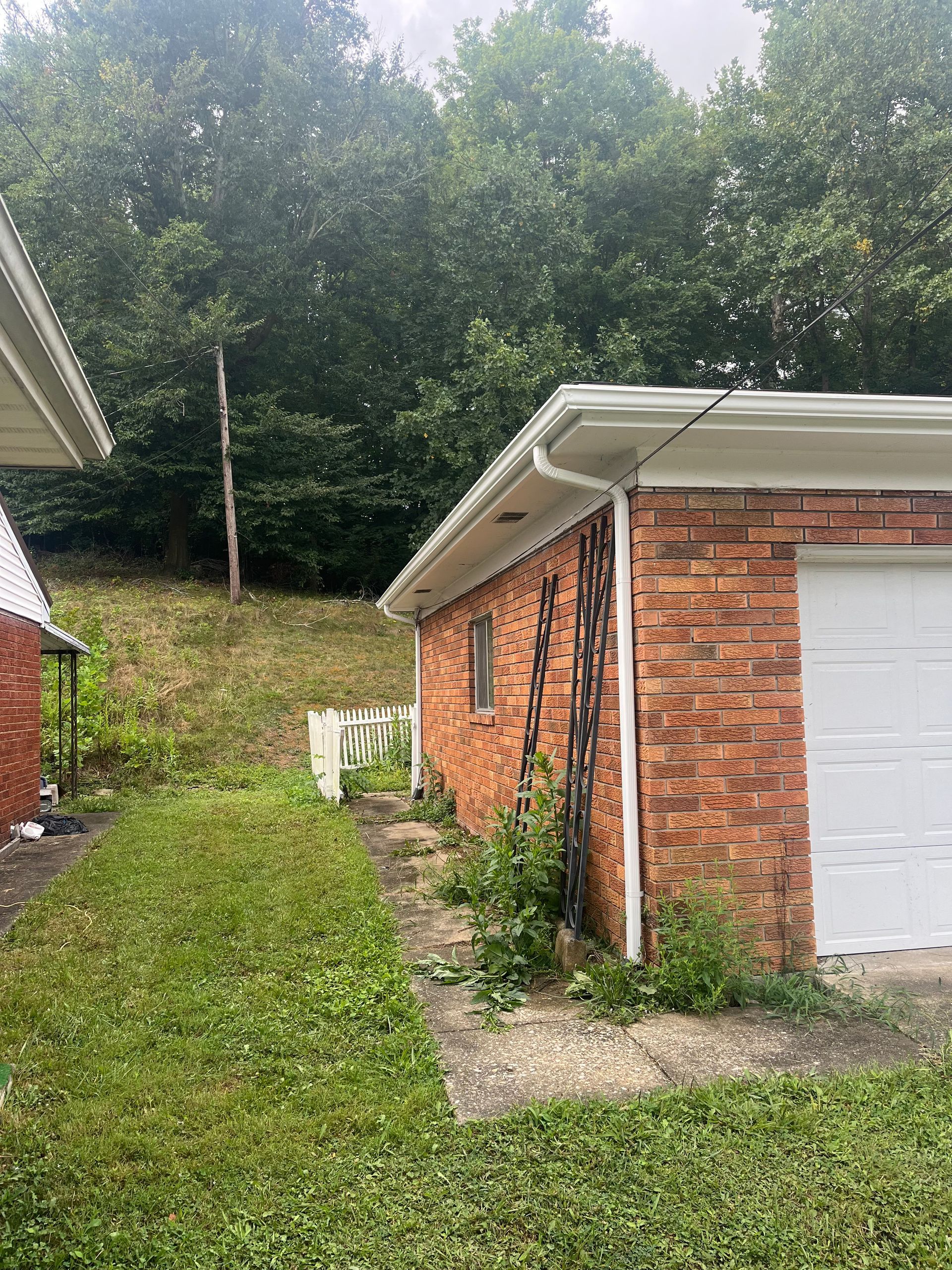 A brick house with a white garage door is sitting on top of a grassy hill.
