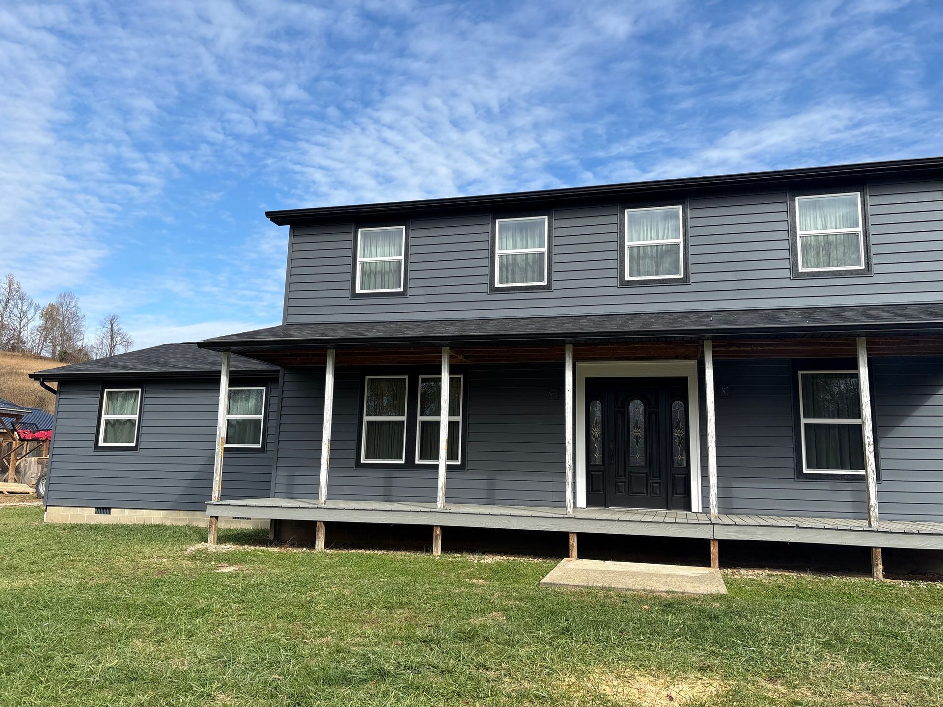 A gray two-story house with a porch and a black front door under a blue sky.