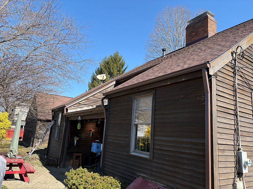 Brown house exterior with chimney, side porch, and red picnic table on a sunny day.