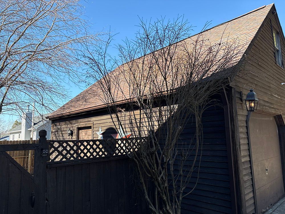 Brick house with a steep roof, leafless trees, and a black fence under a clear blue sky.