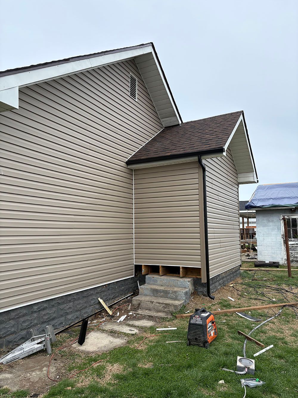 Side view of a beige house with a small porch and yard debris during construction or repair.