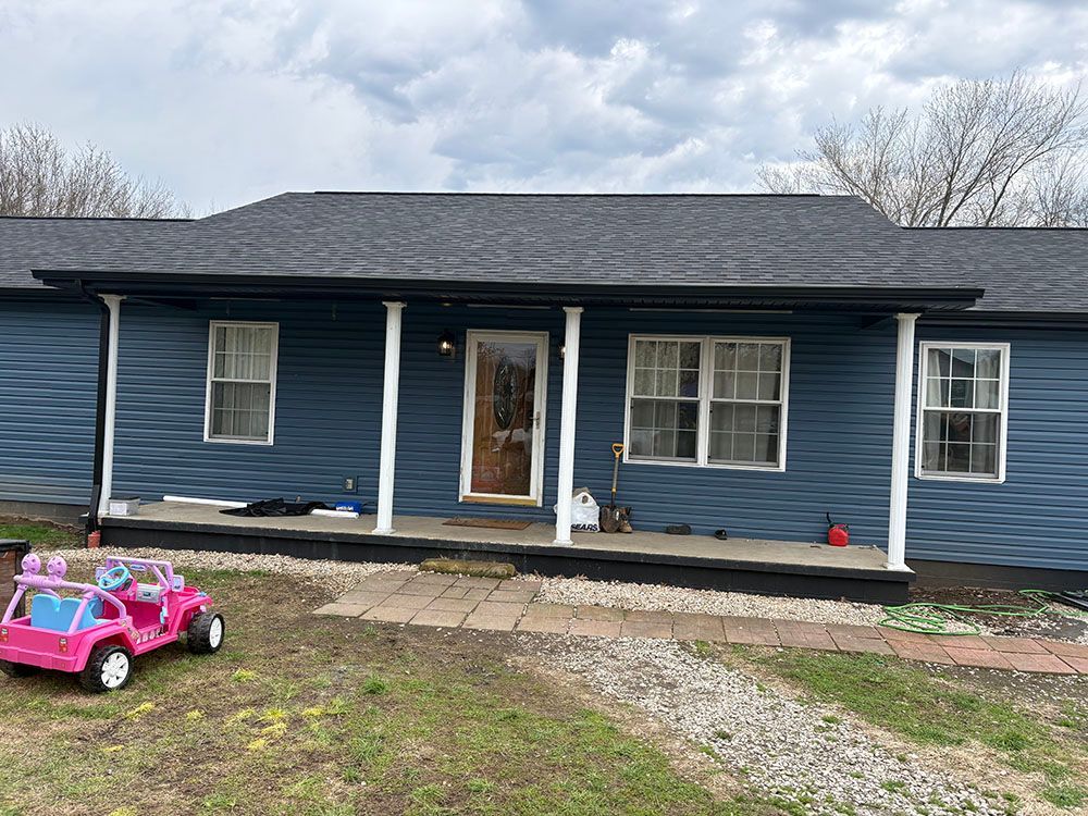 Blue single-story house with a porch and a pink toy car in the front yard.