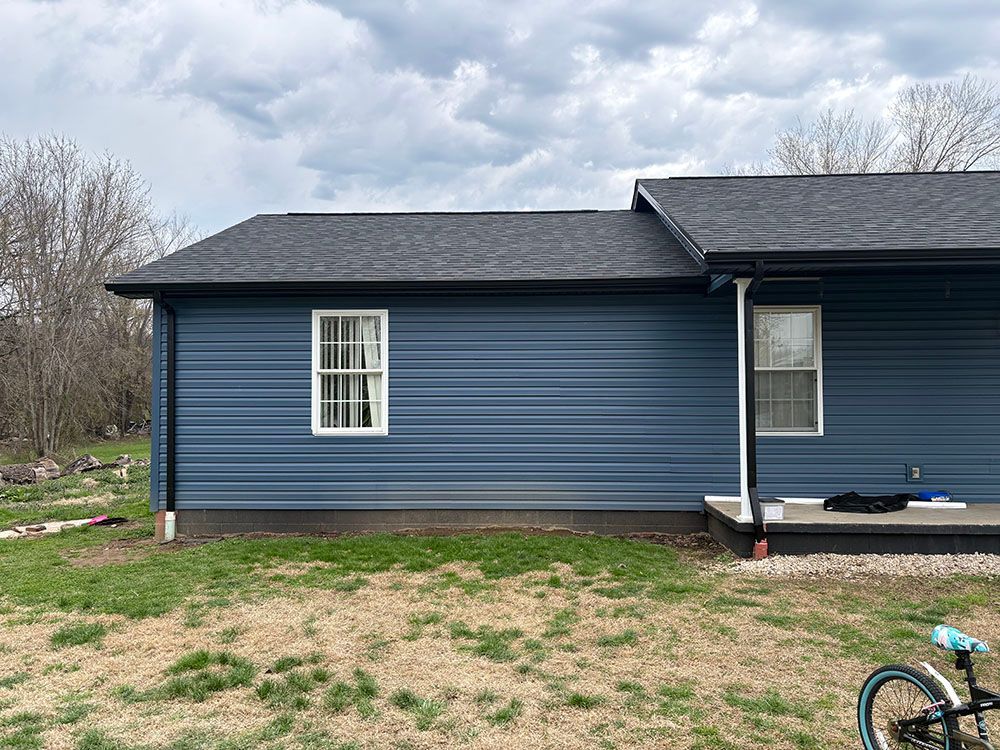 Blue house exterior with small windows, patchy grass yard, and cloudy sky.