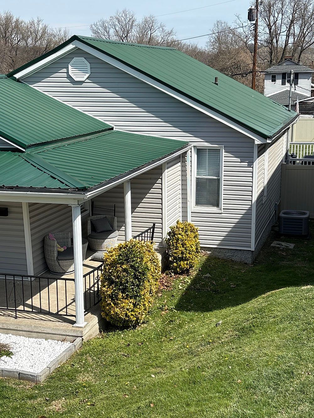 Row of gray houses with green metal roofs on a grassy hillside under a clear sky.