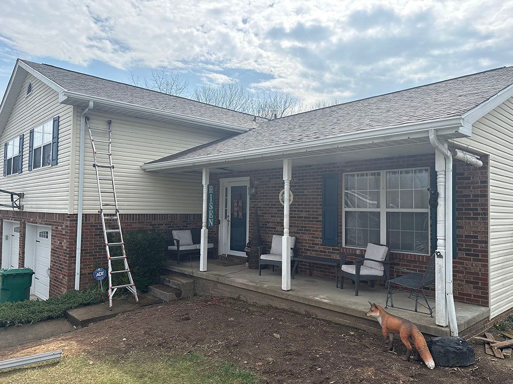 House exterior with covered patio, ladder, and a dog standing in the yard.