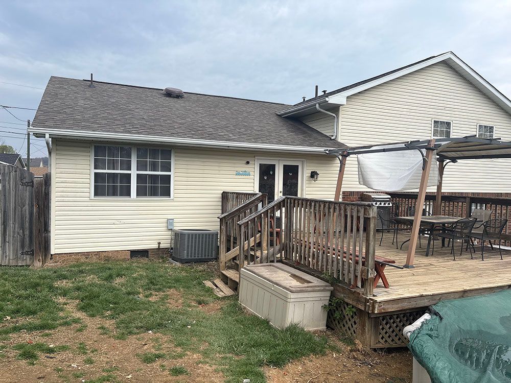 Backyard view of a beige house with a wooden deck, patio furniture, and an air conditioner unit.