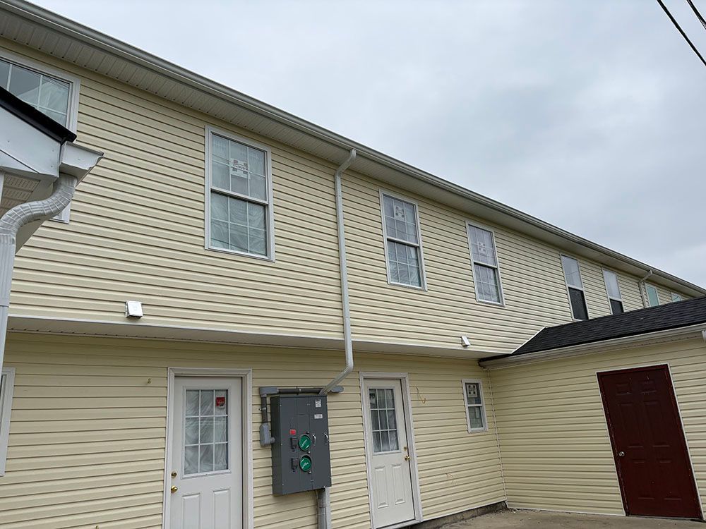 Two-story beige apartment building with white doors and windows under a cloudy sky.