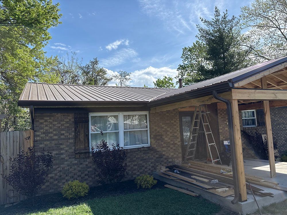 Brick house exterior with metal roof, front porch, and ladder under a covered carport.