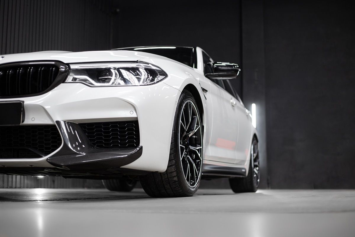 White BMW M5 with black accents in a dark garage, angled low to the ground.