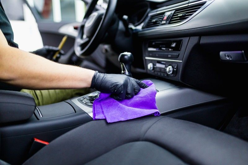 Person wearing gloves wiping a car's dashboard with a purple cloth.