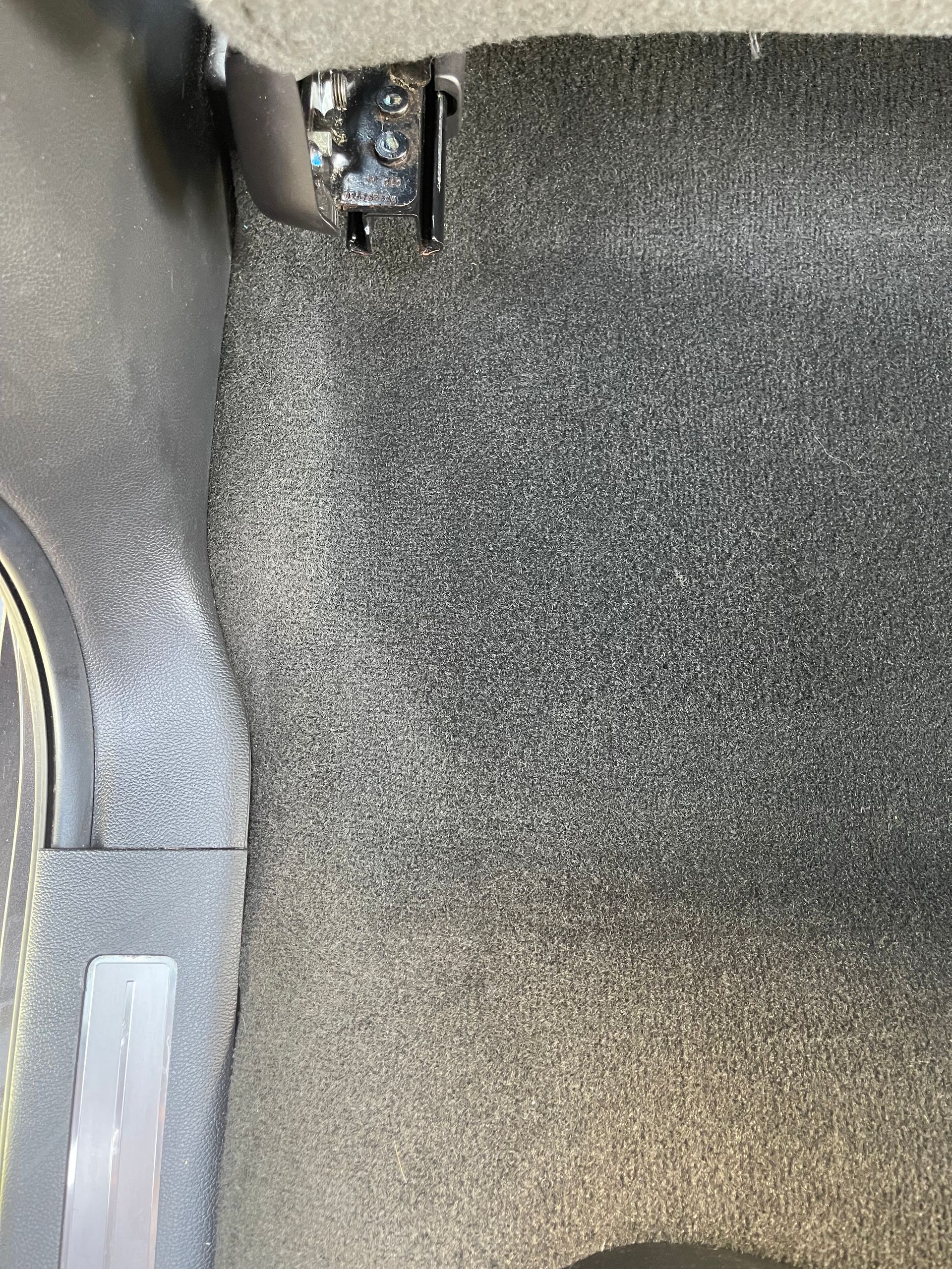 Gray carpeted car interior, close-up view, with a black metal bracket visible.