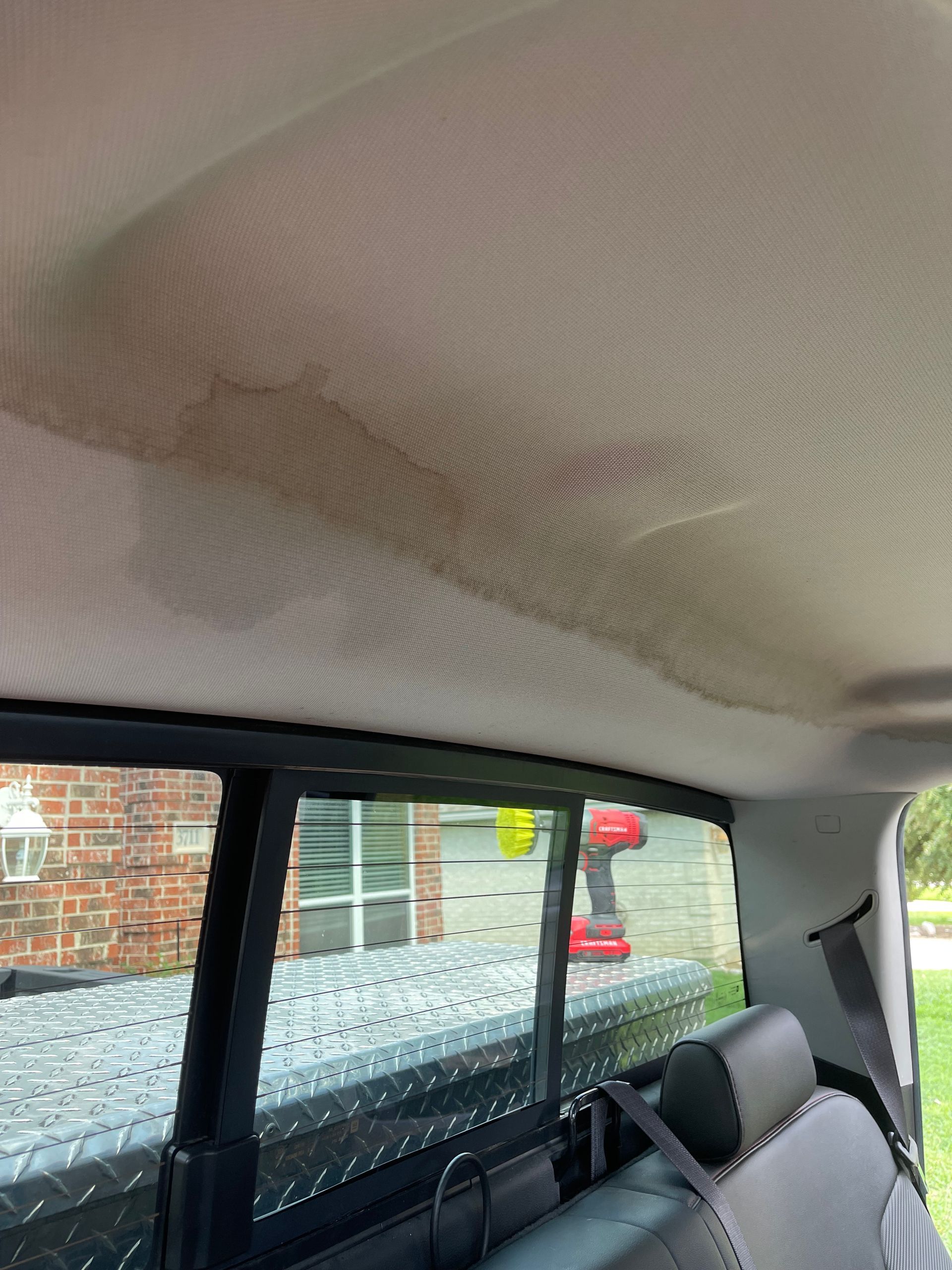 Stained car ceiling, likely water damage, above the rear window and seat. Truck bed visible outside.