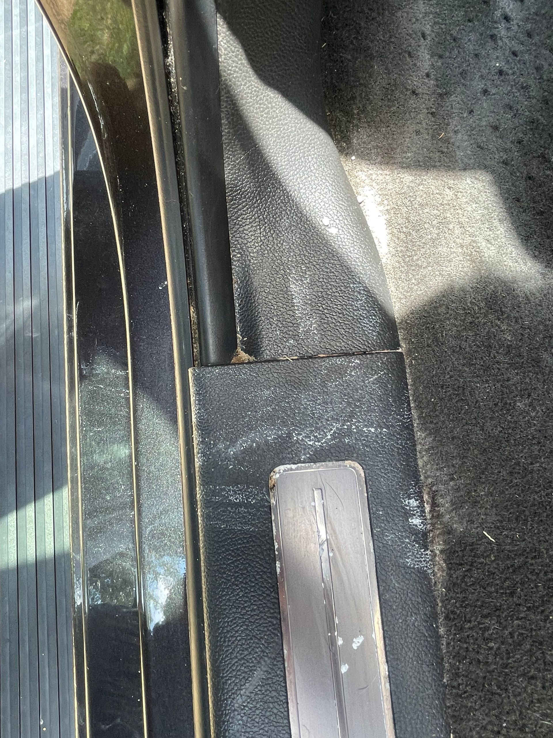 Black car interior, showing a step and trim with scuff marks, plus carpet.